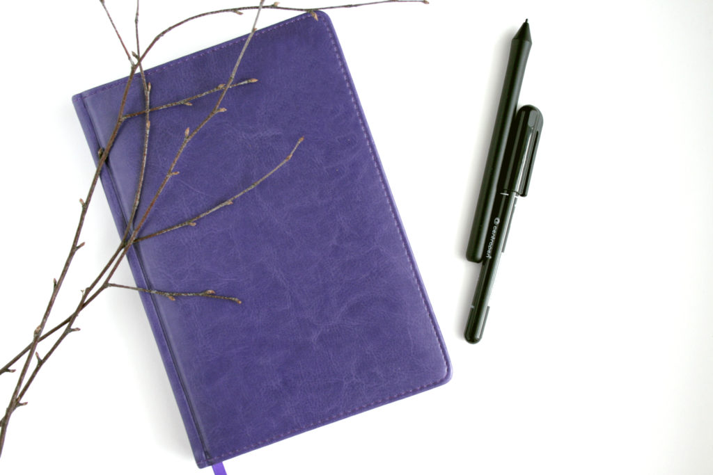 A picture of a notebook or journal with a writing pen. 