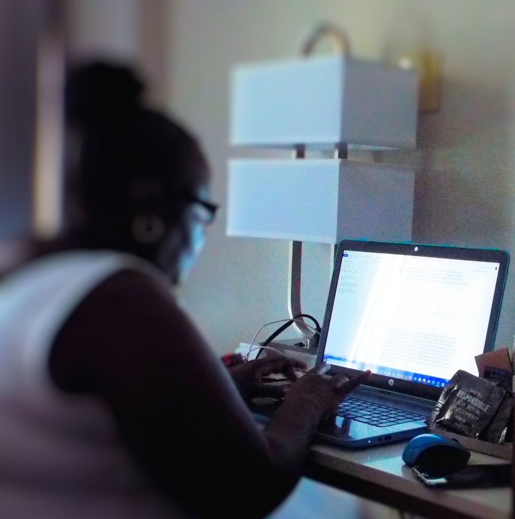 Janice Elliott-Howard sitting at the desk in hotel room creating a chapter to depict how a few words become a story.